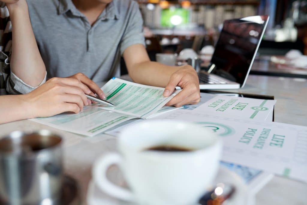 Close-up shot of unrecognizable young family sitting at cafe table and reading life insurance brochure