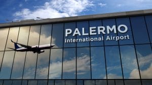 Airplane silhouette landing in Palermo, Sicily, Italy. City arrival with airport direction signboard and sunset in background. Trip and transportation