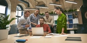 Business professionals at work. Multicultural team, group of young cheerful business people analyzing data, looking at laptop screen while working together in the office