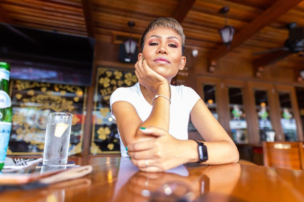 Kuala Lumpur, Malaysia: January 7, 2022: Portrait of a pretty smiling Malaysian woman, sitting at a table in a café in Kuala Lumpur, Malaysia. A young charming Asian girl sitting alone at a wooden table in a restaurant.