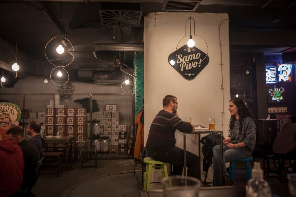 BELGRADE, DECEMBER 4, 2021: Selective blur on two young adults, man and woman, discussing and drinking in Samo Pivo, a craft beer bar in the city center of Belgrade, Serbia.