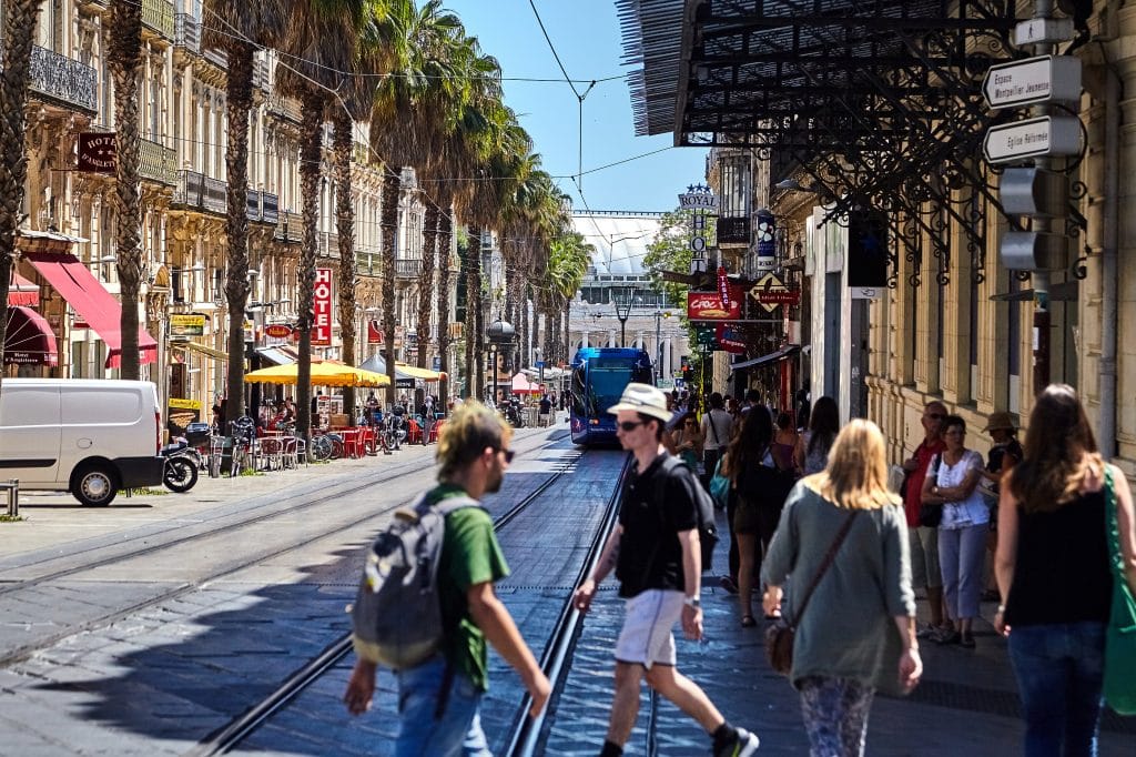 MONTPELLIER, FRANCE - June 24, 2015: People crossing the road through tram ways. View of a city street with residents, tourists, green palm trees and beautiful old buildings
