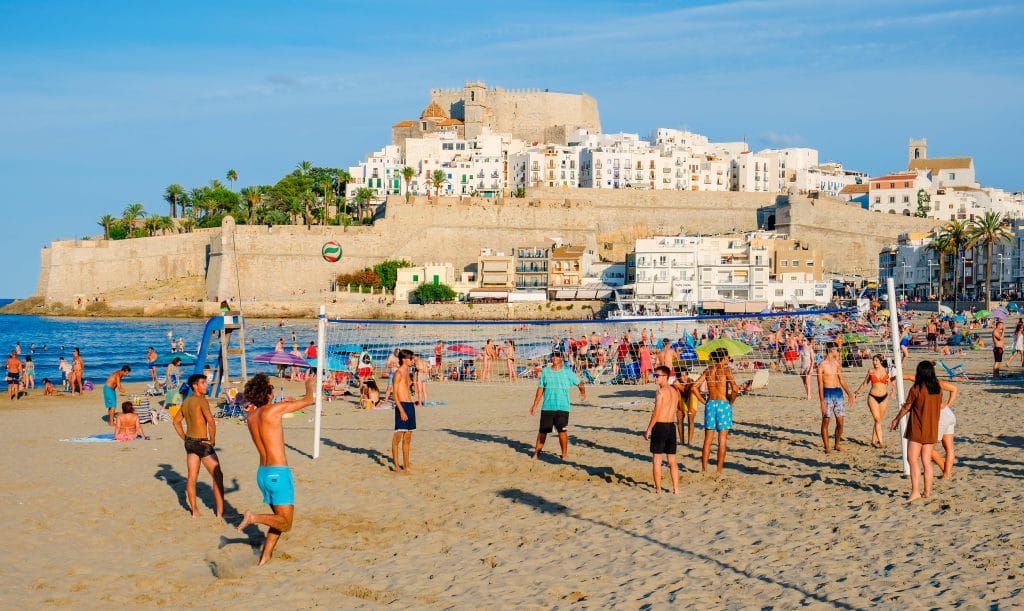 PENISCOLA, SPAIN - AUGUST 2, 2021: People enjoying on the beach in Peniscola, in Valencia, highlighting its fortified walls on the background. It is an important summer tourist destination in Spain