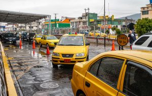 Quito, Ecuador - December 2, 2008: Yellow Taxi stand and ride-up outside Mariscal Sucre International airport. Plenty of cars, green buildings other side of street under silver rainy sky.