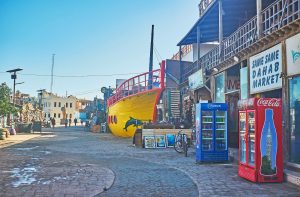 DAHAB, EGYPT - DECEMBER 25, 2017: The wide street is lined with stores and cafes of the market, one of the restaurants is designed like the ship, on December 25 in Dahab.