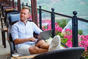 An Emotional Man Sits At The Computer On Vacation And Works. Fre
