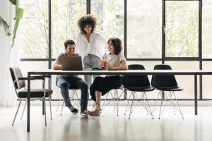 Group of young coworkers looking at laptop in spacious bright loft coworking space