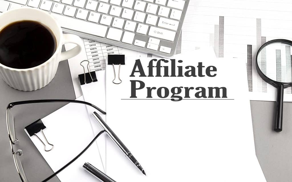 AFFILIATE PROGRAM text on a paper with magnifier, coffee and keyboard on a grey background