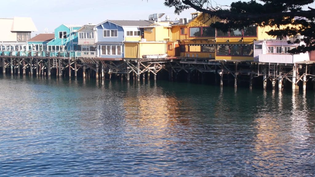 Colorful wooden houses on piles, pillars or pylons, ocean sea water, historic Old Fishermans Wharf, Monterey bay or harbor, California coast USA. Tourist beachfront promenade, waterfront boardwalk.