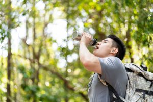 Asian Handsome Man Backpacker Drinking Bottle Of Water In Forest