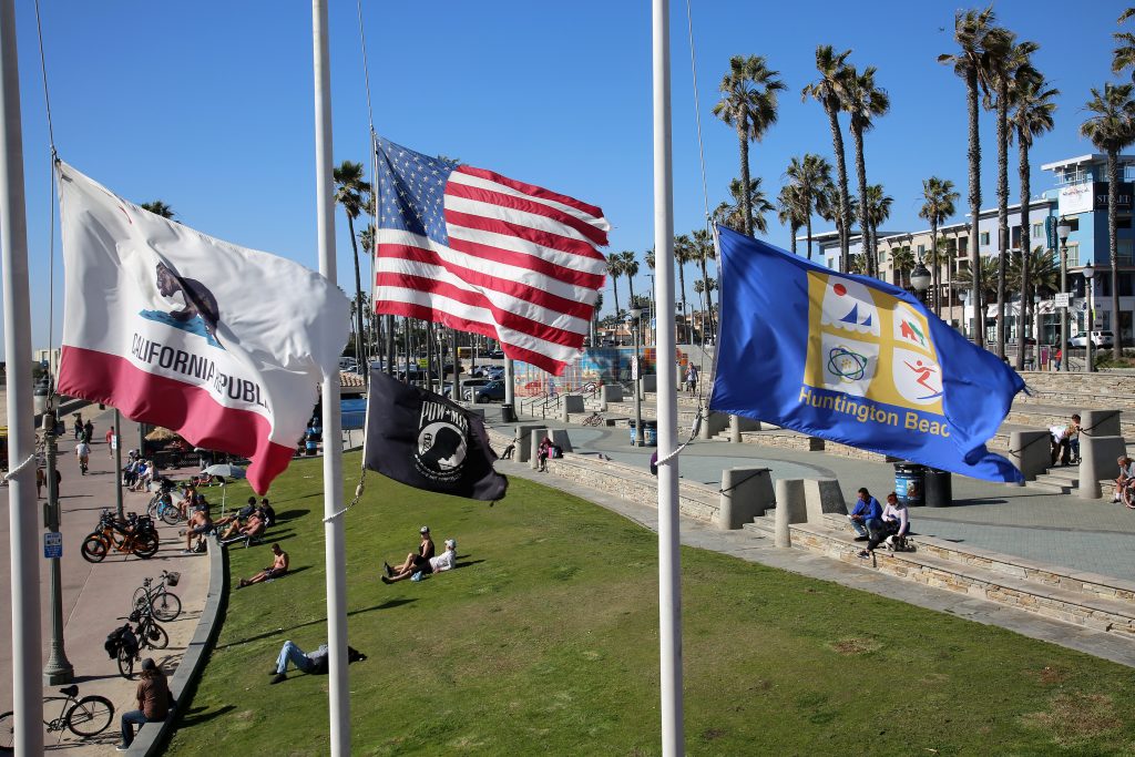 Huntington Beach, California - USA - February 25, 2021: California, American, POW, Huntington Beach Flags fly at Half Mast in Surf City with People enjoying the sunshine in the background. Editorial.